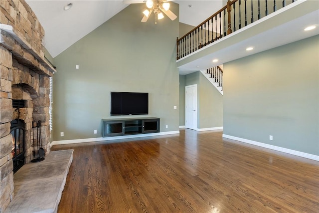 unfurnished living room with baseboards, stairway, a stone fireplace, wood finished floors, and a ceiling fan