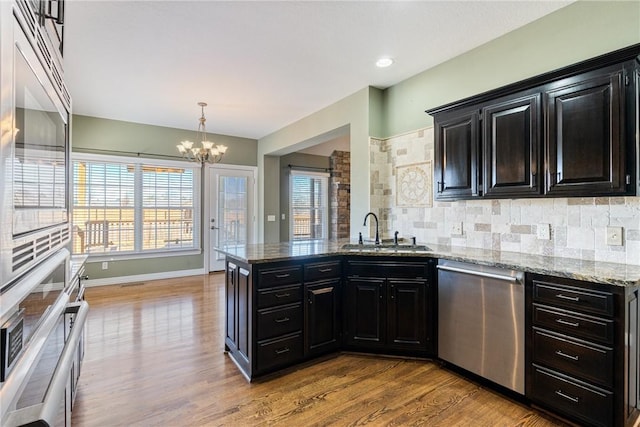 kitchen featuring a sink, stainless steel appliances, light wood-style floors, dark cabinets, and backsplash