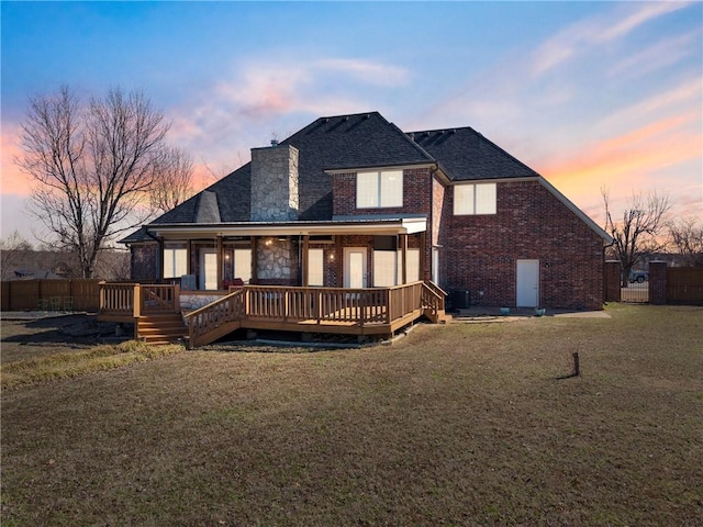 back of property featuring brick siding, central AC, a lawn, a chimney, and a deck