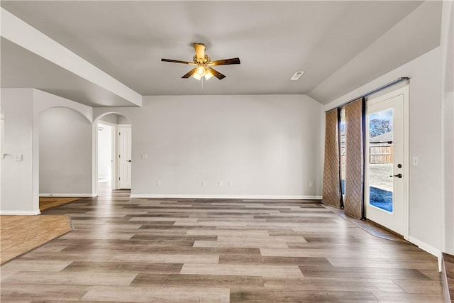 interior space with a ceiling fan, wood finished floors, baseboards, lofted ceiling, and arched walkways