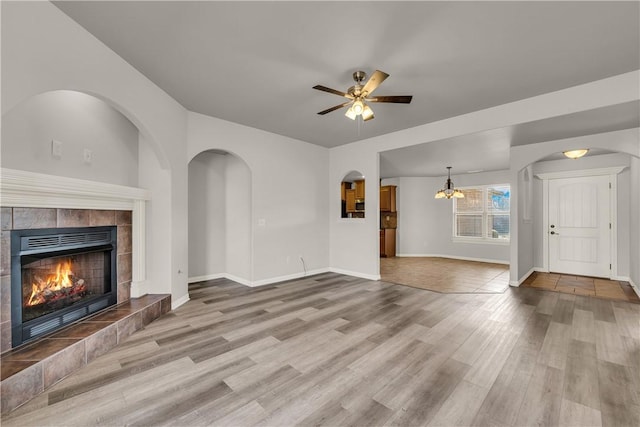 unfurnished living room with baseboards, wood finished floors, a fireplace, and ceiling fan with notable chandelier