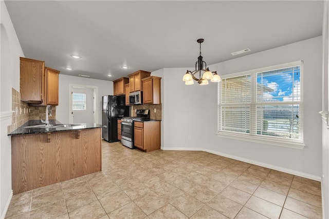 kitchen featuring baseboards, brown cabinets, appliances with stainless steel finishes, a peninsula, and an inviting chandelier