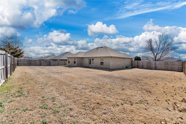 back of house with brick siding, a fenced backyard, and a lawn