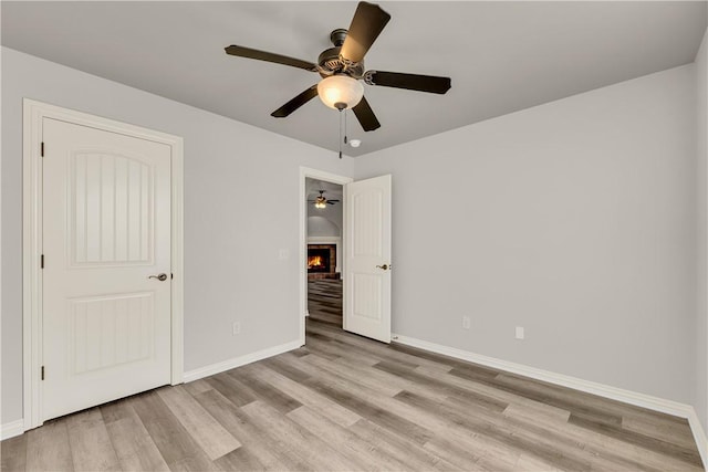 unfurnished bedroom with ceiling fan, baseboards, light wood-style flooring, and a fireplace