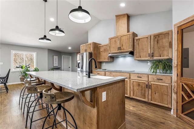 kitchen featuring a sink, under cabinet range hood, stainless steel fridge, black electric cooktop, and a kitchen island with sink