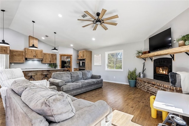 living area featuring visible vents, a ceiling fan, wood finished floors, lofted ceiling, and a brick fireplace