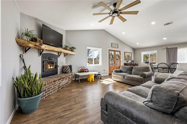 living room featuring wood finished floors, visible vents, baseboards, lofted ceiling, and a fireplace