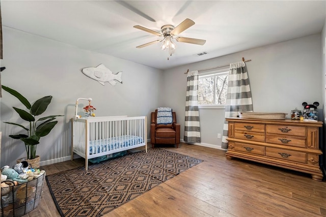 bedroom with visible vents, a crib, baseboards, hardwood / wood-style flooring, and a ceiling fan