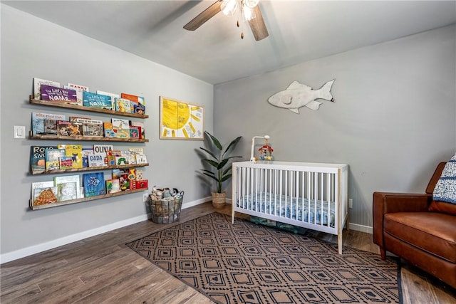 bedroom featuring a crib, a ceiling fan, baseboards, and wood finished floors