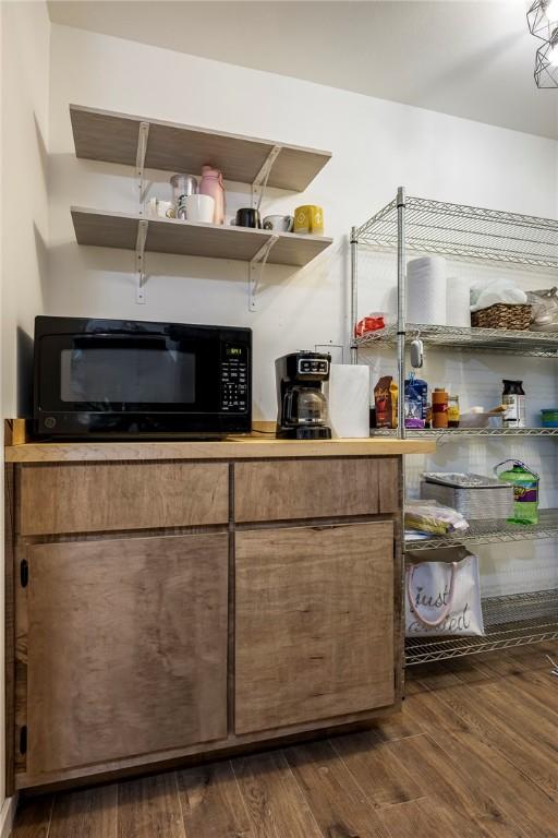 interior space with open shelves, brown cabinetry, dark wood-style flooring, and black microwave