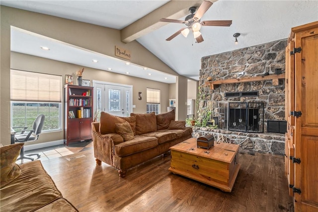 living area with wood finished floors, visible vents, a ceiling fan, vaulted ceiling with beams, and a stone fireplace