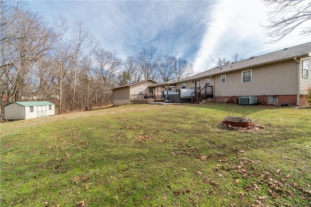 view of yard featuring a wooden deck, an outdoor fire pit, central AC, a storage shed, and an outbuilding