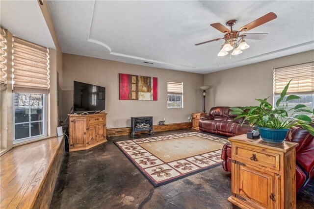 living room featuring a wealth of natural light, a wood stove, and ceiling fan