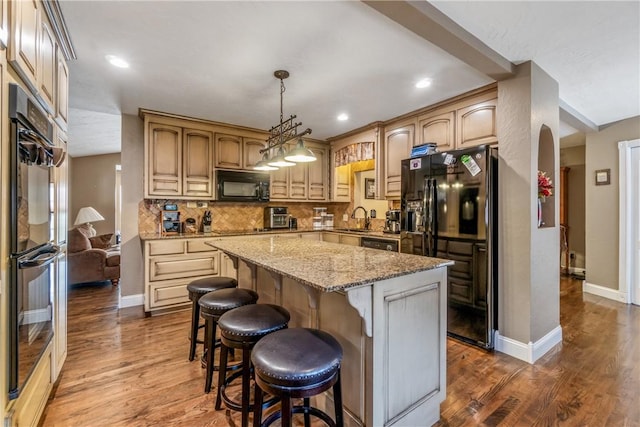 kitchen with black appliances, light stone counters, tasteful backsplash, wood finished floors, and a center island