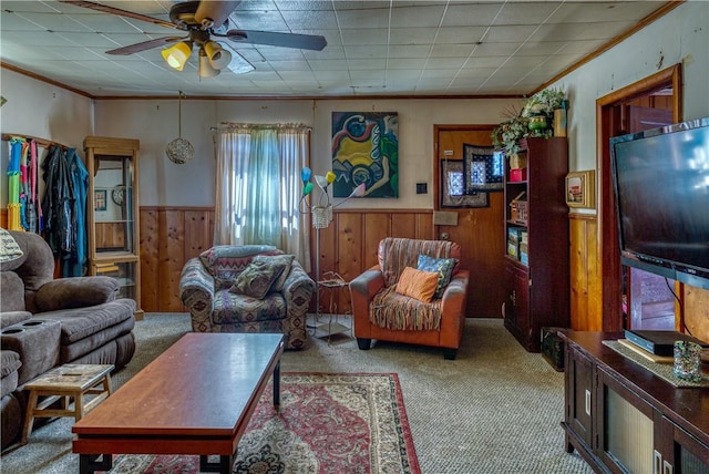 carpeted living area with wooden walls, wainscoting, crown molding, and ceiling fan