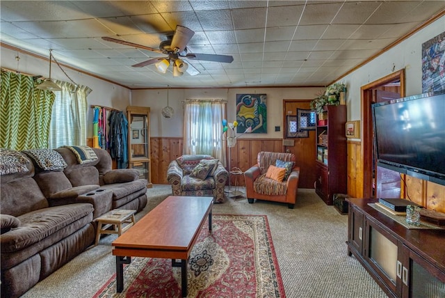 living room featuring wooden walls, a ceiling fan, wainscoting, ornamental molding, and light carpet