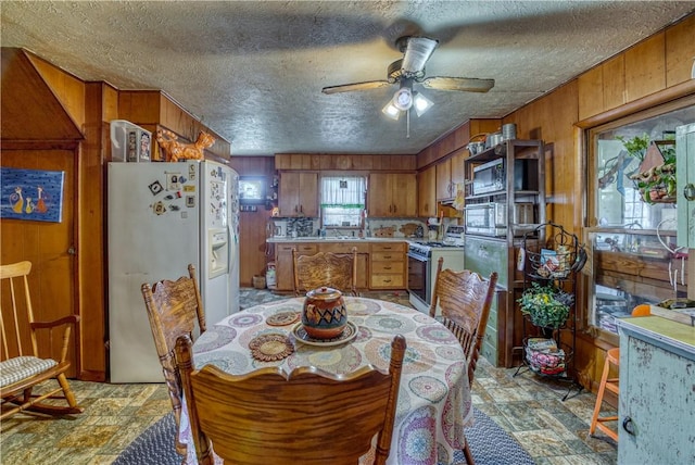 kitchen featuring brown cabinetry, light countertops, gas range oven, wood walls, and white fridge with ice dispenser