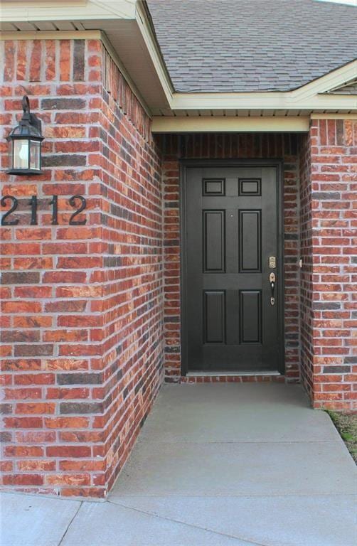 doorway to property with brick siding and roof with shingles