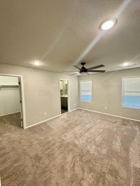 unfurnished bedroom featuring a walk in closet, a textured ceiling, ensuite bath, carpet flooring, and baseboards