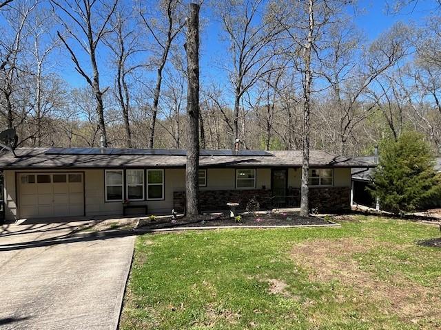 view of front of property with a garage, solar panels, concrete driveway, and a front yard