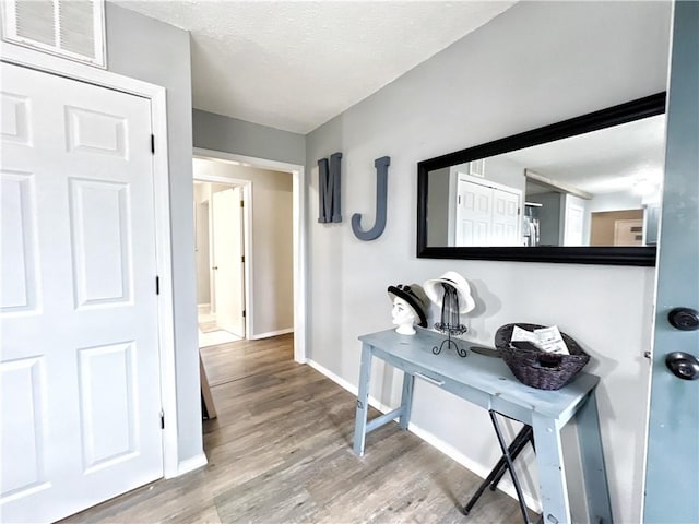 corridor featuring visible vents, a textured ceiling, baseboards, and wood finished floors