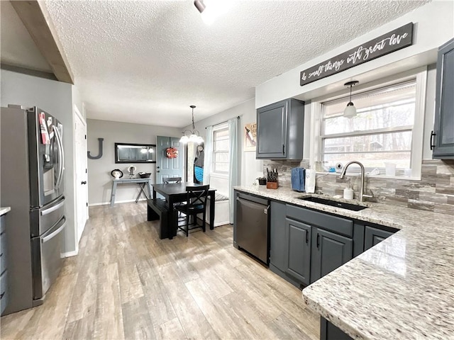 kitchen featuring tasteful backsplash, light stone countertops, appliances with stainless steel finishes, light wood-style floors, and a sink