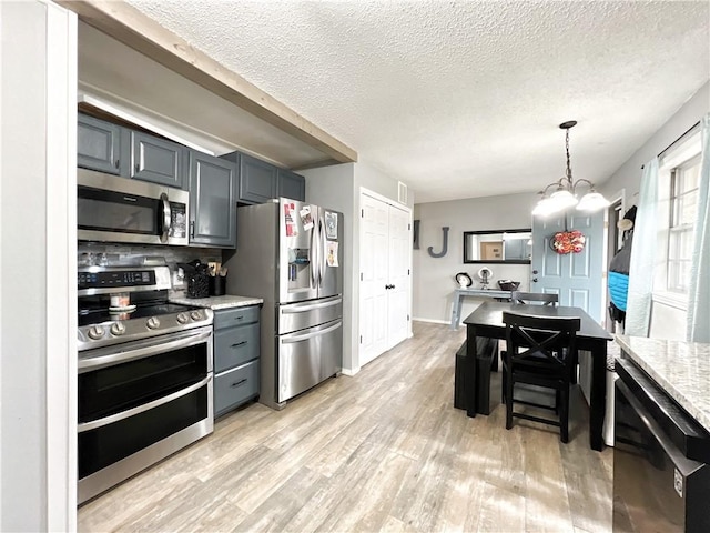 kitchen with decorative light fixtures, a textured ceiling, appliances with stainless steel finishes, light wood finished floors, and a chandelier