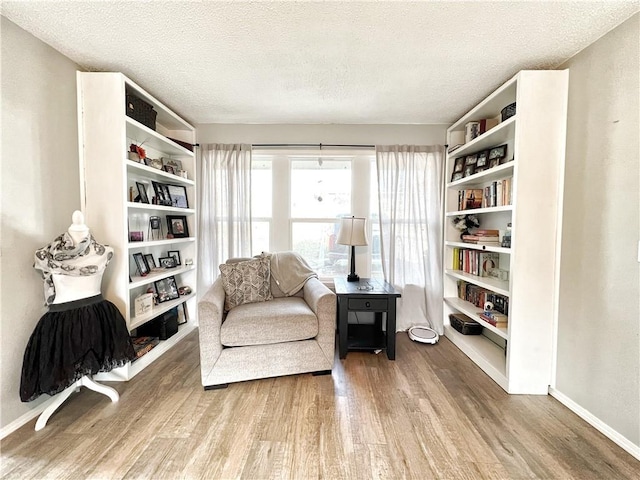 living area featuring a textured ceiling, baseboards, and wood finished floors