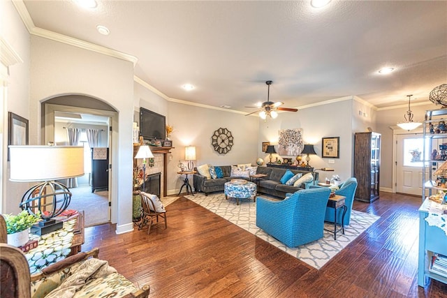 living area featuring baseboards, a tiled fireplace, ornamental molding, hardwood / wood-style floors, and a ceiling fan