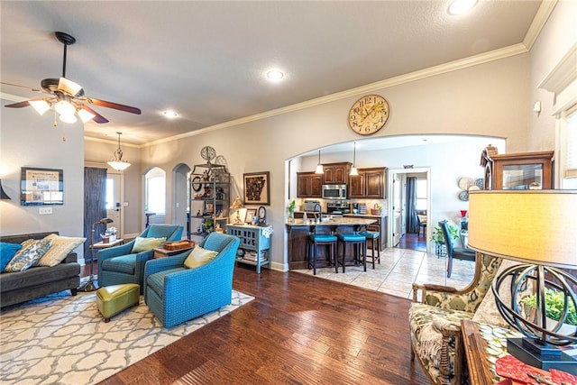 living area featuring crown molding, a ceiling fan, arched walkways, and light wood finished floors