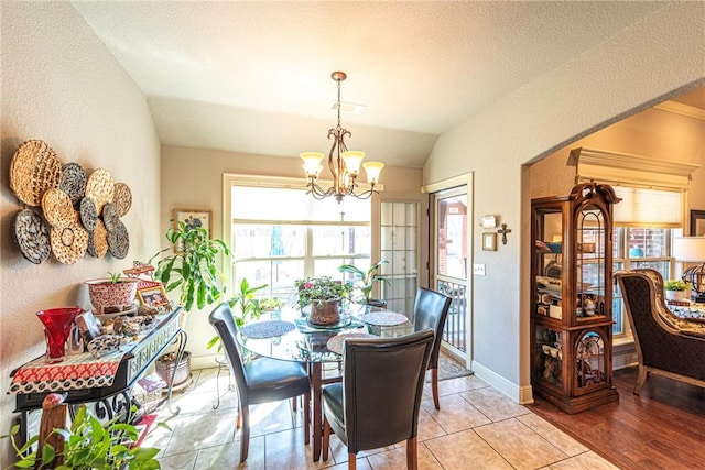 dining space featuring baseboards, a chandelier, vaulted ceiling, a textured wall, and a textured ceiling