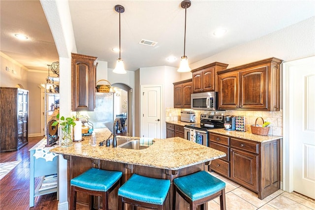 kitchen with visible vents, a sink, arched walkways, appliances with stainless steel finishes, and a breakfast bar area