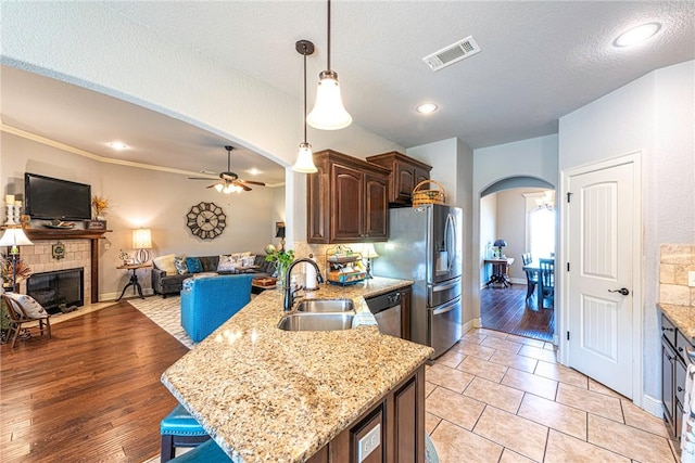 kitchen with visible vents, arched walkways, stainless steel appliances, a sink, and a tiled fireplace