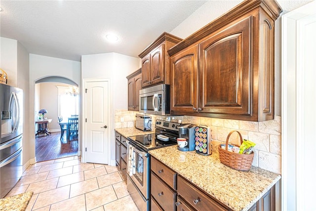 kitchen with arched walkways, appliances with stainless steel finishes, tasteful backsplash, and light stone counters