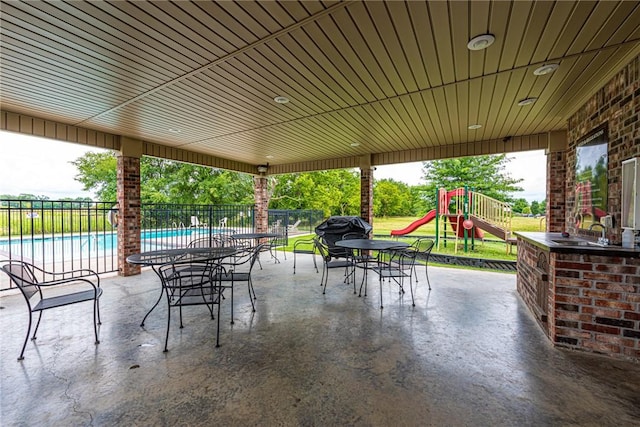 view of patio / terrace with area for grilling, fence, playground community, and a community pool