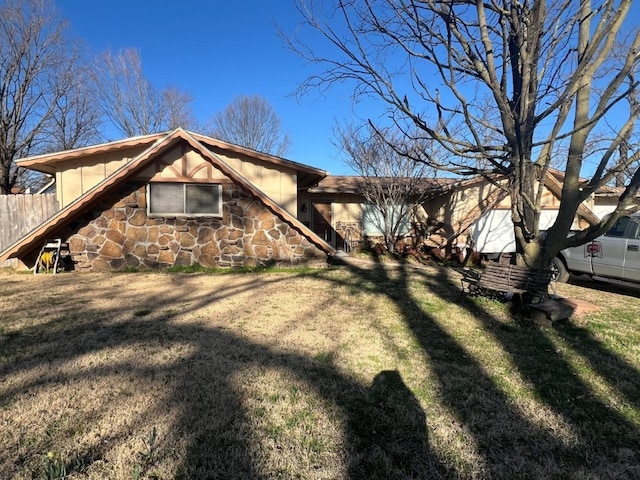 view of front facade with stone siding, a yard, and fence