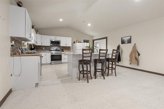 kitchen featuring a breakfast bar, lofted ceiling, stainless steel appliances, white cabinetry, and tasteful backsplash