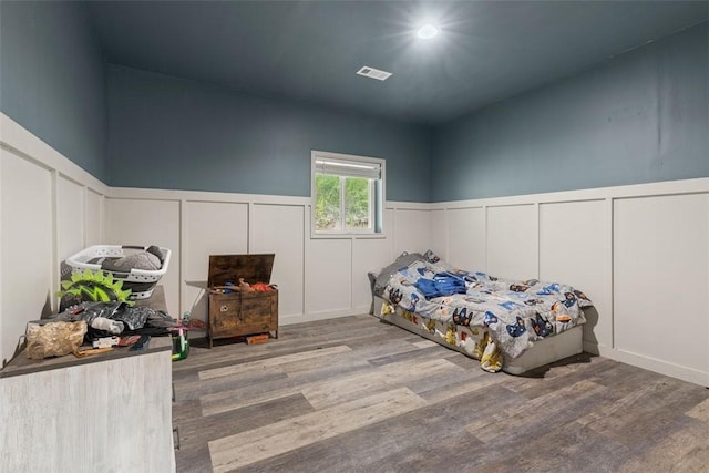 bedroom with a decorative wall, wood finished floors, visible vents, and wainscoting