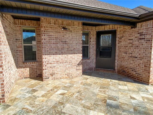 entrance to property featuring a patio area, brick siding, and roof with shingles