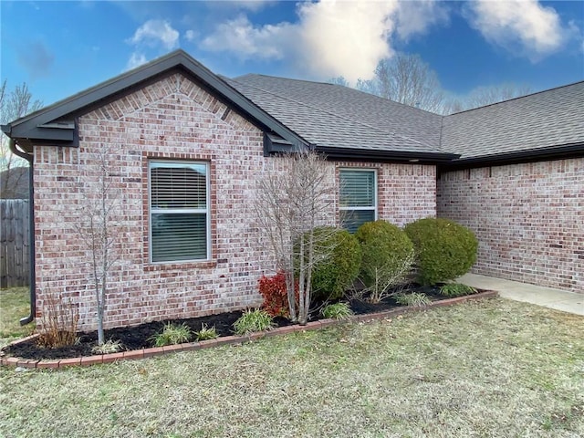 view of front of house with fence, brick siding, a front lawn, and a shingled roof