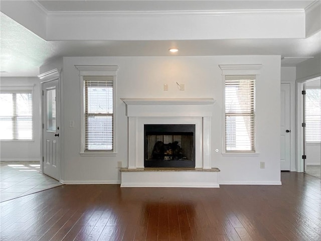 unfurnished living room featuring a fireplace with raised hearth, ornamental molding, baseboards, and hardwood / wood-style floors