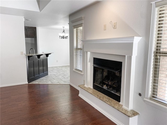 living room featuring a fireplace with raised hearth, an inviting chandelier, baseboards, and wood finished floors