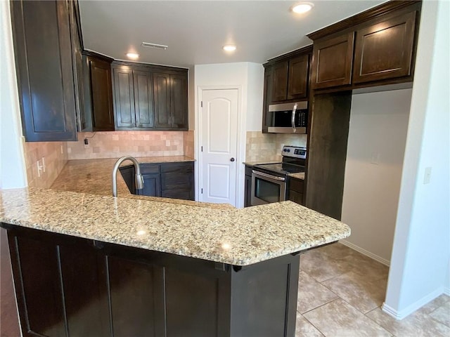 kitchen with dark brown cabinets, stainless steel appliances, light stone counters, and a peninsula