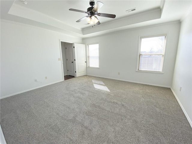 empty room featuring a tray ceiling, baseboards, visible vents, and crown molding