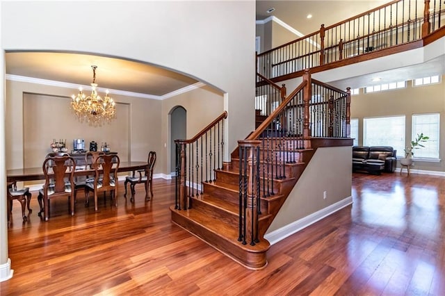 stairway with wood finished floors, baseboards, arched walkways, ornamental molding, and a notable chandelier