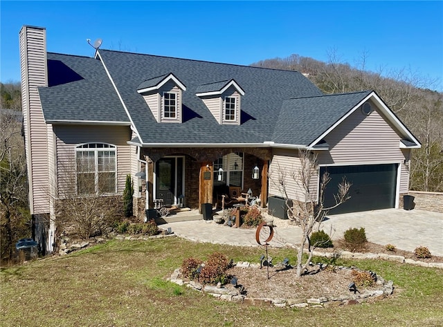 view of front of house featuring roof with shingles, an attached garage, covered porch, a chimney, and concrete driveway