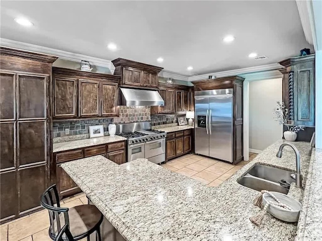 kitchen with a sink, dark brown cabinetry, appliances with stainless steel finishes, wall chimney range hood, and backsplash