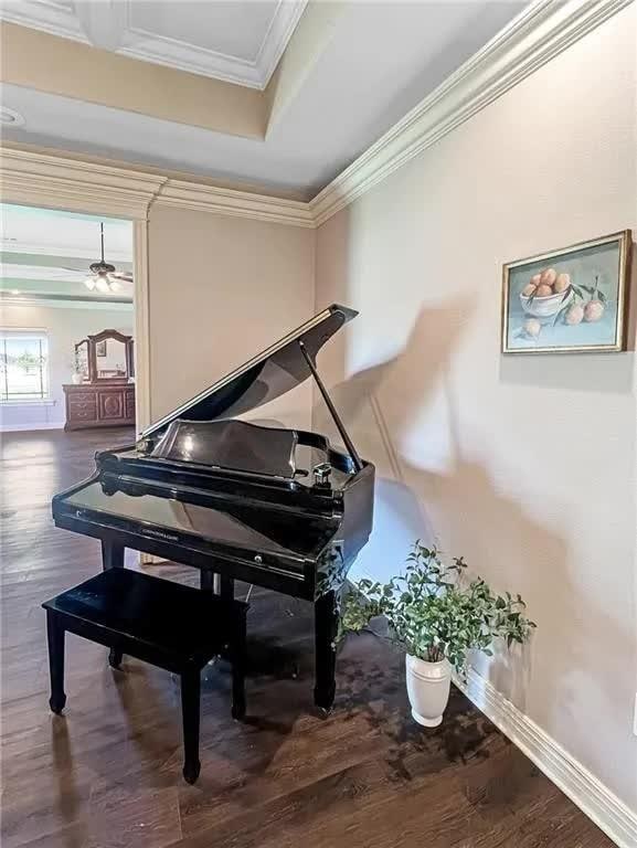 living area with crown molding, wood finished floors, baseboards, and a raised ceiling