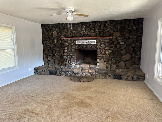 unfurnished living room featuring ceiling fan, carpet flooring, a fireplace, and a textured ceiling