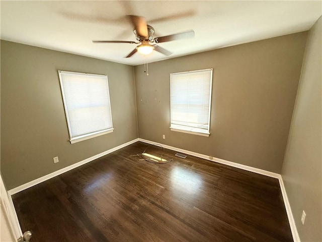 unfurnished room with visible vents, a healthy amount of sunlight, baseboards, and dark wood-style flooring